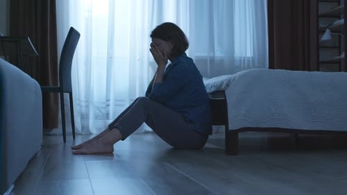 Lonely and sad woman sits in a dark room. The concept of a person in a state of depression or stress