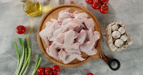 Alitas de pollo crudas en una tabla de cortar con tomates girados