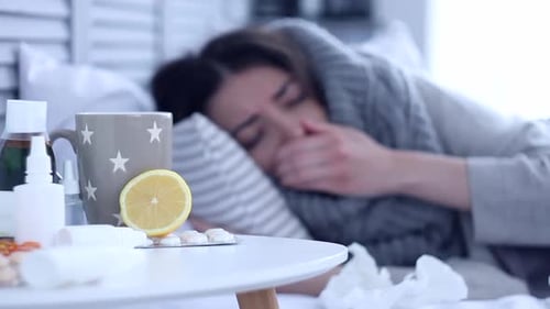 Sick woman lying on bed with flu at grey bedroom