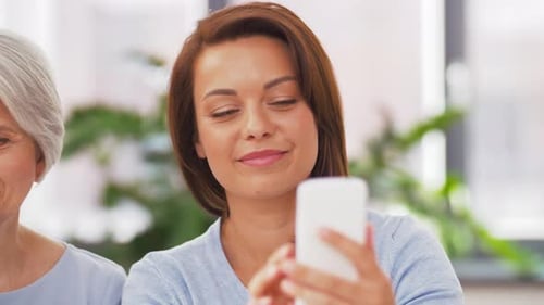 Smiling Woman and Senior Look at Cell Phone