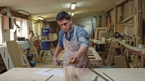 Young Adult Measures Wood in Workshop