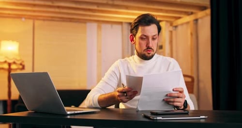 Elegant Concentrated Caucasian Male Looks Over Some Paperwork Sit at Work Space Next to Loft