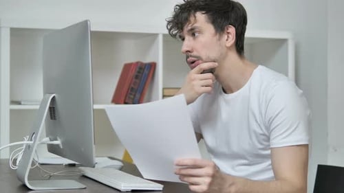 Pensive Young Creative Man Reading Documents, Brainstorming at Work