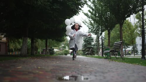 Girl Running with Balloons Jumps over Puddle in Rain