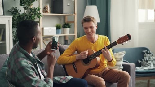 Man Plays Guitar for Friend on Couch