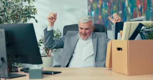 Senior Man Celebrating at Desk with Box