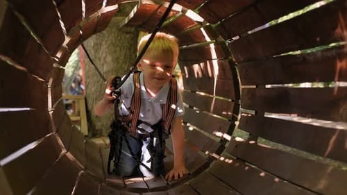 Little Boy Passes Obstacles in a Rope Park He Climbs Through a Wooden Tunnel