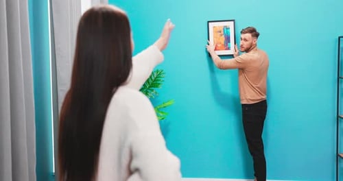 Young Adults Hanging Wall Art Together at Home