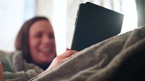 Woman in Bed Smiling At Tablet