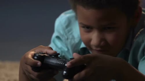 Junge mit gemischter Rasse, der mit Play Station-Steuerung auf dem Boden liegt und Videospiele spielt