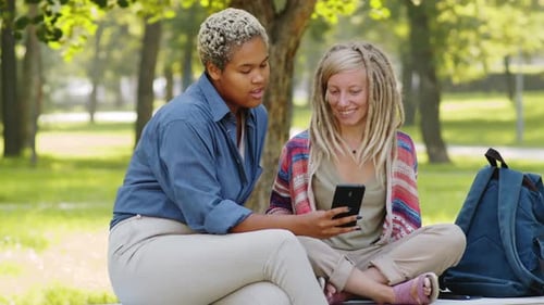 Diverse Female Students Using Smartphone, Smiling and Talking in Park