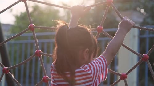Nettes kleines Mädchen klettert auf Seilnetz auf Spielplatz. Glückliches kleines Mädchen, das Spaß auf dem Spielplatz
hat