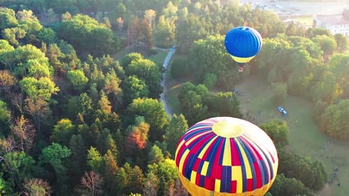 Beautiful sunbeams illuminate the balloons that fly over the park, green trees.