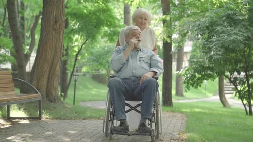 Woman Pushing Man in Wheelchair Through Sunny Park