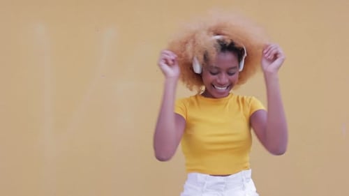 Woman Dancing with Headphones Against Yellow Background
