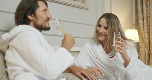 Affectionate Couple Toasting with Champagne Lying on Their Bed. Hotel, Travel, Relationships and