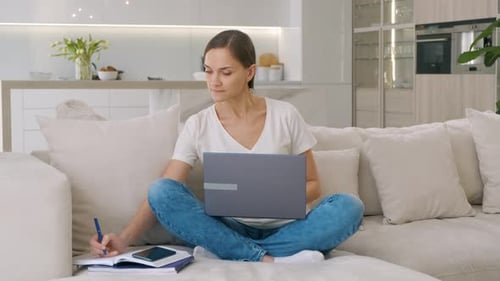 Woman Works on Laptop and Writes in Notebook