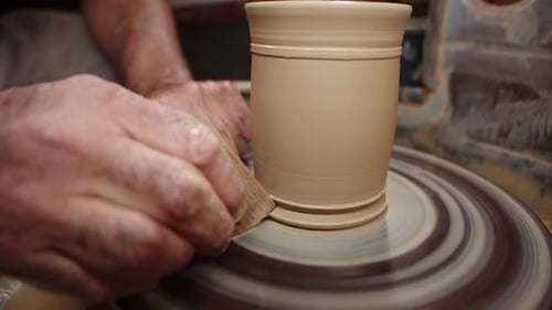 Potter professionnel a formé une cruche en argile avec un grattoir spécial sur le tour de potier et enlève ses mains