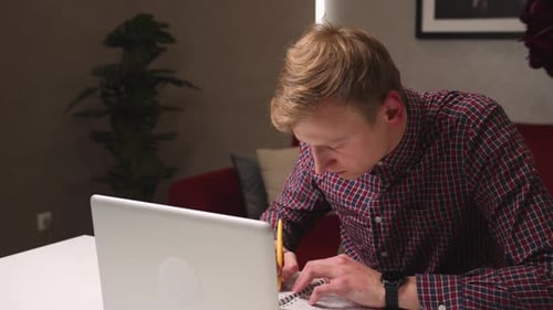 Young Adult Taking Notes From Laptop Indoors