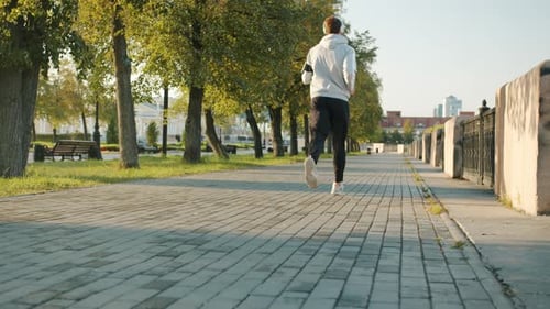 Slow Motion Back View of Guy in Sportswear Running Outdoors in Urban Street