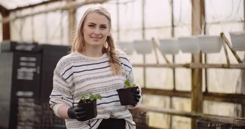 Smiling Woman Holding Plants in Greenhouse