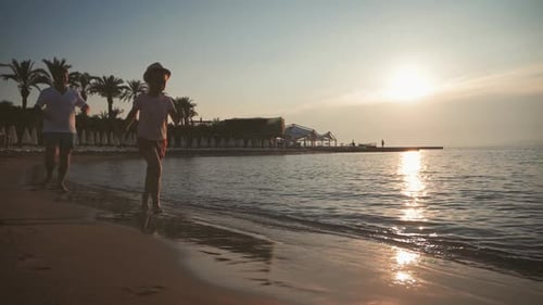 Silhouette des Vaters und seiner kleinen Tochter rennen bei Sonnenuntergang glücklich ins Meer