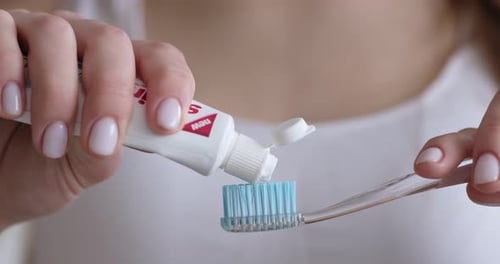 Woman Squeezing Toothpaste on Toothbrush at Home