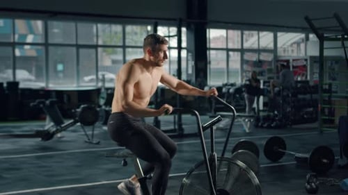 Shirtless Man Exercises on Stationary Bike at Gym