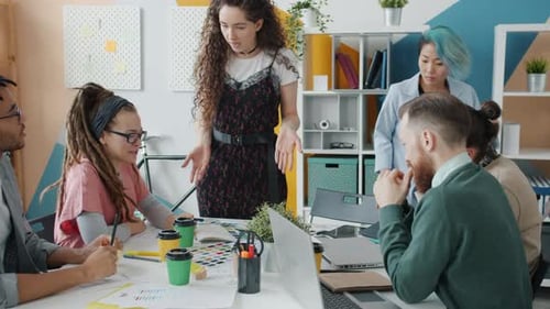 Young Woman Talking To Group of Creative Designers Sharing Ideas on Project in Office