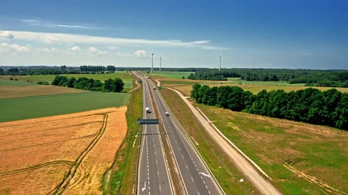Aerial view of golden field and wind turbines near highway.