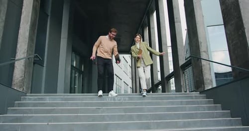Hombre y mujer bajando las escaleras en el centro urbano de la ciudad en un elegante estilo de negocios informal, hablando