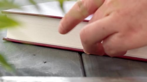Female Hands Take Red Hard Cover Book on Wooden Table Close Up