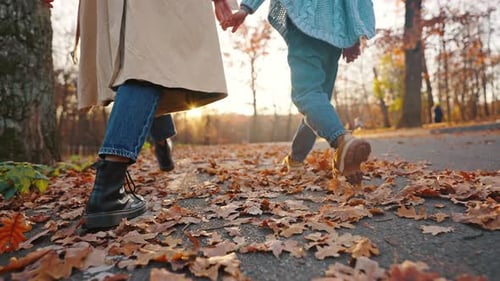 Unknown Mom Holding Hand of Little Daughter Walking in Autumn Park