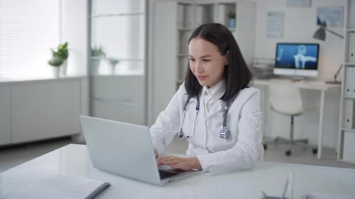 Smiling Doctor Works on Laptop in Office Setting