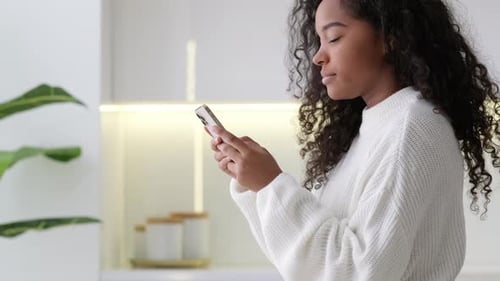Young Woman Using Smartphone in Bright Kitchen