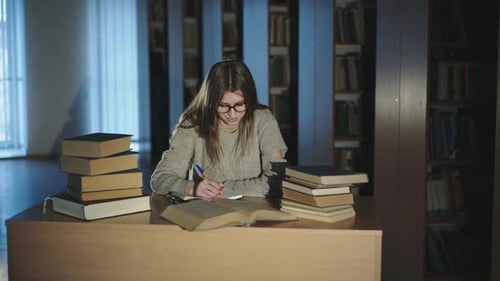A Young Girl Diligently Notes Information From Books in the Library Late