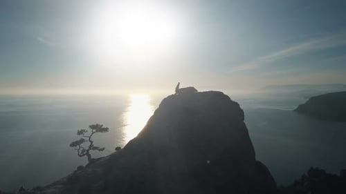 Aerial Silhouette of a Young Woman Climbing To the Top of a Mountain Against the Sea at Sunset. Lady