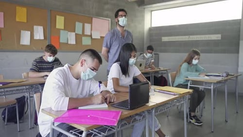 Teacher Wearing Face Mask Walks in the Classroom Explaining Lesson to Class of Teenager Students