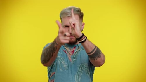 Young Adult Making Finger Gun Gesture on Yellow Background