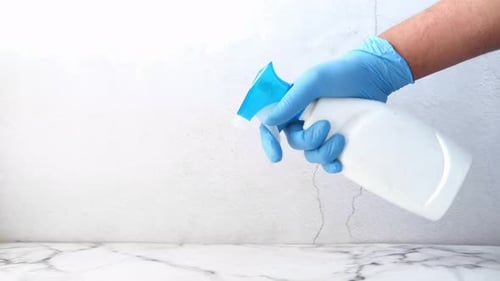 Spraying Disinfectant with Blue Gloves on Marble Surface