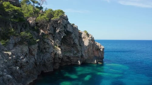 Drone Flight Over Rocky Coastline With Trees And Blue Tranquil Sea