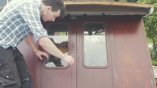 Man climbs into vintage motorboat cabin in countryside