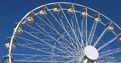 White Ferris Wheel Rotating Against Clear Blue Sky
