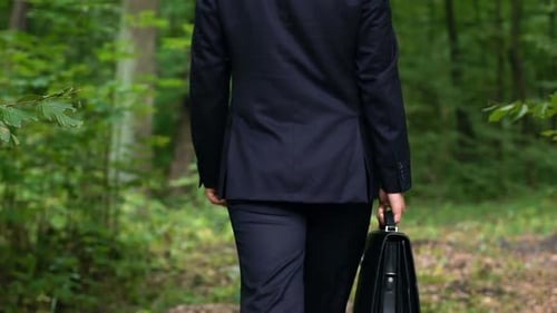 Junger Geschäftsmann, der mit Aktentasche im Park spaziert, Arbeit beendet, Freiheit