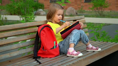 Young Girl Drawing on Park Bench with Backpack
