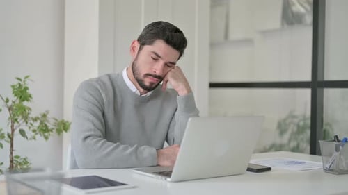 Müder junger Mann macht Nickerchen, während er mit Laptop im Büro sitzt