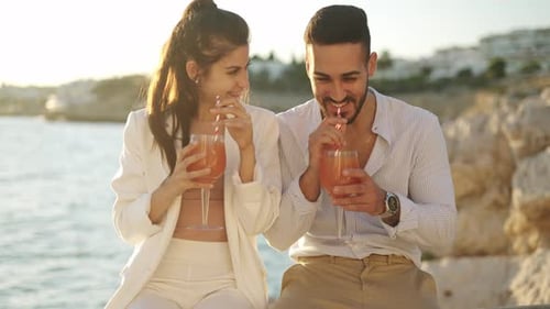 Content Ethnic Couple Drinking Cocktails and Talking on Embankment