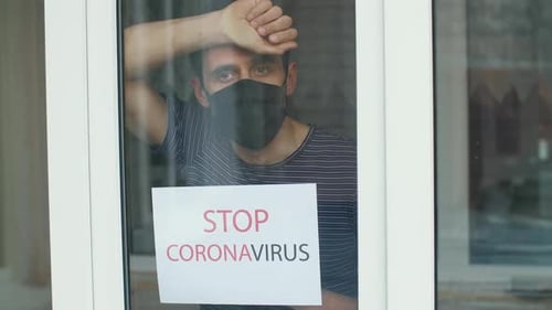 Adult Wearing Mask Leans Against Door with Sign