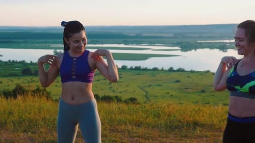 Women Exercising Shoulders on Hill at Sunset