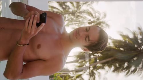 Vertical Video Portrait of Smiling Young Man Stands Outdoors at Hotel Resort Near Pool and Using App